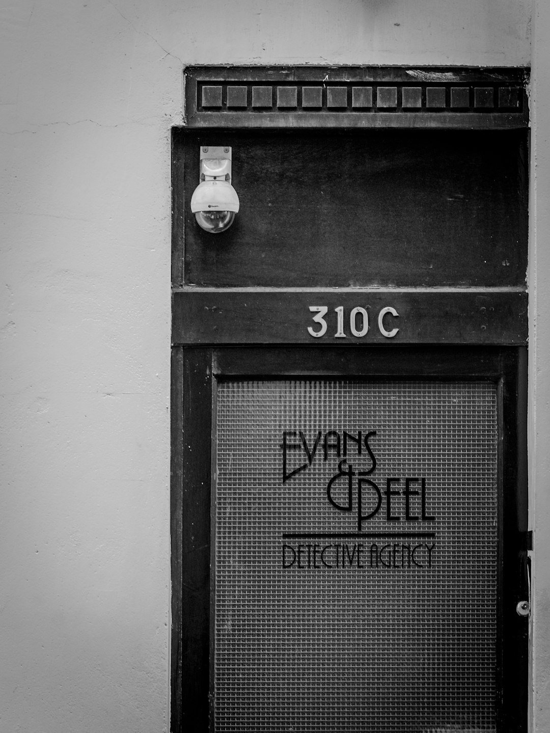 Black and white photo of a detective agency door labeled 'Evans & Peel' at address 310C. It has a vintage style, conveying mystery.